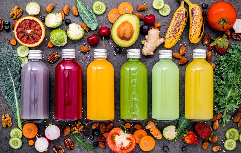 bottles of assorted brightly colored juices surrounded by nutritional foods