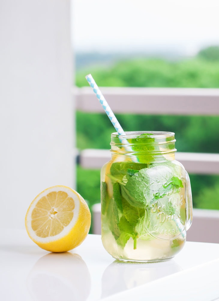 cut lemon next to mason jar of lemonade with garnishes and a straw