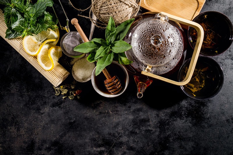 bird eye view of dark counter and tea pot with honey, lemons, and herbs