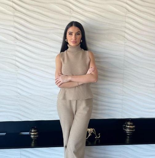 Woman with arms crossed wearing tan sleeveless turtleneck suit