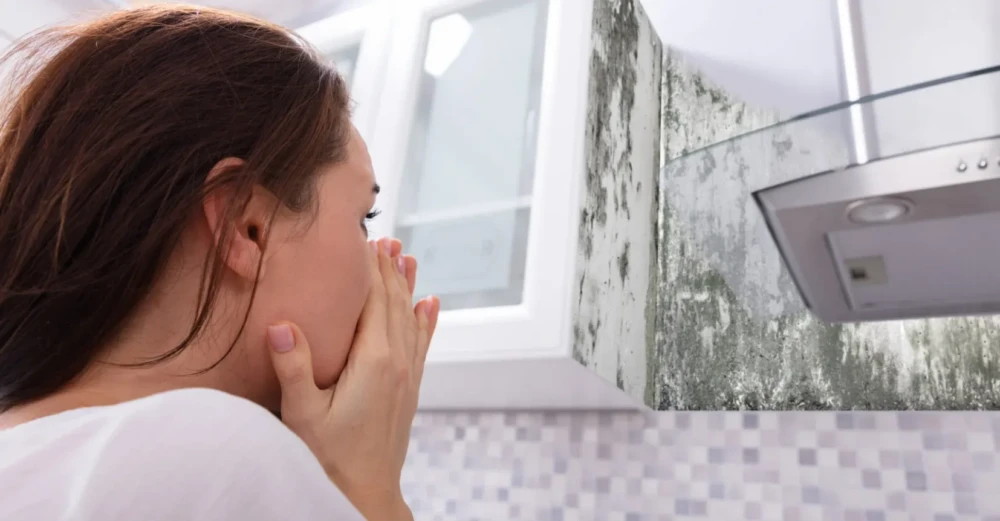 Woman covering her mouth while looking at visible mold growth on an indoor wall.