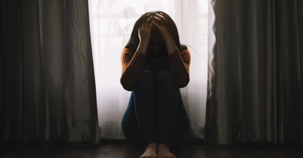 Person sitting on the floor with head in hands, conveying depression or emotional distress.